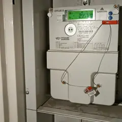 Cyfrowy licznik energii elektrycznej APATOR OTUS 3 z zielonym wyświetlaczem. Widać przewody podłączone do plomby, co może sugerować próby manipulacji, jak oszukać licznik prądu.