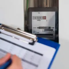 Osoba spisuje odczyt licznika energii elektrycznej. Cyfrowy wyświetlacz pokazuje zużycie w kWh.