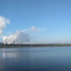 Dymiące kominy elektrowni w Bełchatowie, pokazujące, ile energii produkuje Bełchatów. W tle jezioro i las.