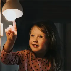 Mała dziewczynka dotyka żarówki, zastanawiając się, jak wysoka będzie faktura za prąd.