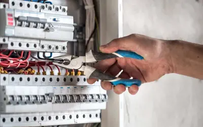 Elektryk przy skrzynce z bezpiecznikami, używa kombinerki do podłączenia przewodów. W ten sposób można włączyć prąd.