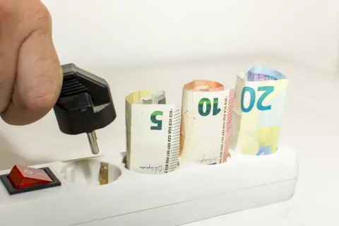 Dłoń z wtyczką, banknoty 5, 10, 20 euro w gniazdkach. Zastanawiasz się, jak zmienić dostawcę energii, by oszczędzać?