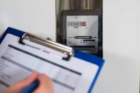 Osoba spisuje odczyt licznika energii elektrycznej. Cyfrowy wyświetlacz pokazuje zużycie w kWh.