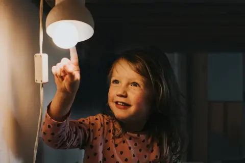 Mała dziewczynka dotyka żarówki, zastanawiając się, jak wysoka będzie faktura za prąd.