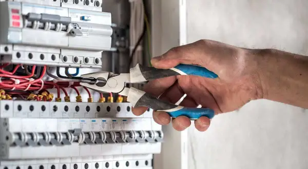 Elektryk z kombinerkami przy skrzynce z bezpiecznikami, przygotowuje się, jak włączyć prąd.