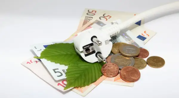 Wtyczka, liście i monety na banknotach euro symbolizują poszukiwanie, gdzie najtańszy prąd.