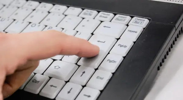 Palec naciska klawisz Enter na klawiaturze laptopa, symbolizując łatwy sposób, jak kupić prąd przez internet.