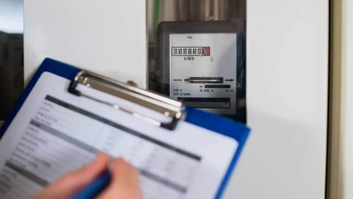 Osoba spisuje odczyt licznika energii elektrycznej. Cyfrowy wyświetlacz pokazuje zużycie w kWh.