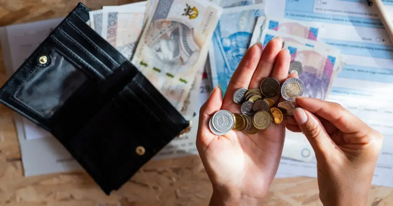 Dłonie liczą monety i banknoty, przygotowując się na obniżkę za prąd. Obok leży otwarty portfel.
