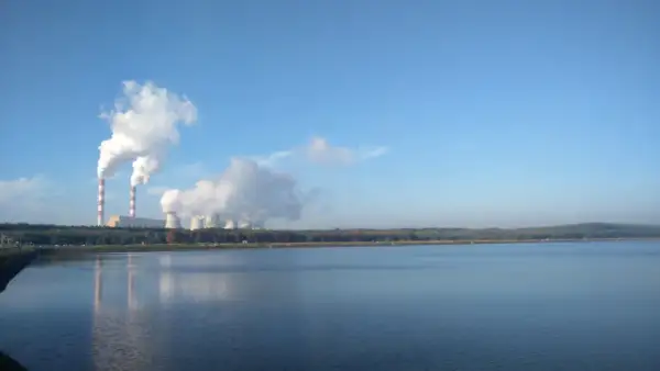 Dymiące kominy elektrowni w Bełchatowie, pokazujące, ile energii produkuje Bełchatów. W tle jezioro i las.